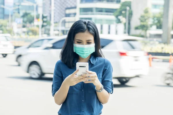 Ασιατικές γυναίκα φοράει μια μάσκα και χρησιμοποιεί ένα τηλέφωνο — Φωτογραφία Αρχείου
