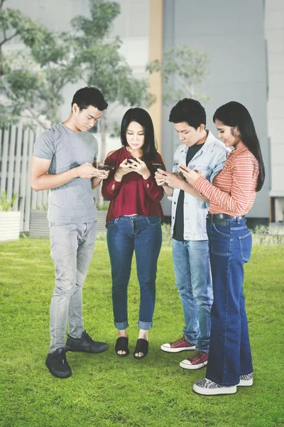 Cuatro jóvenes usan teléfono móvil en el parque —  Fotos de Stock