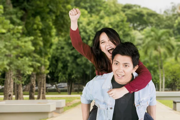 Man giving his girlfriend piggyback ride in the park — Stock Photo, Image