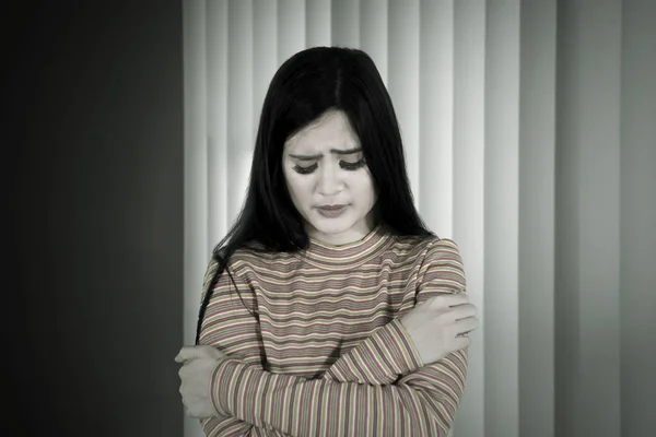 Νεαρή γυναίκα φαίνεται λυπημένη στο σκοτεινό δωμάτιο — Φωτογραφία Αρχείου