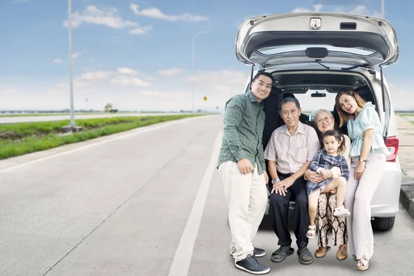 Расширенная счастливая семья сидит на багажнике автомобиля — стоковое фото