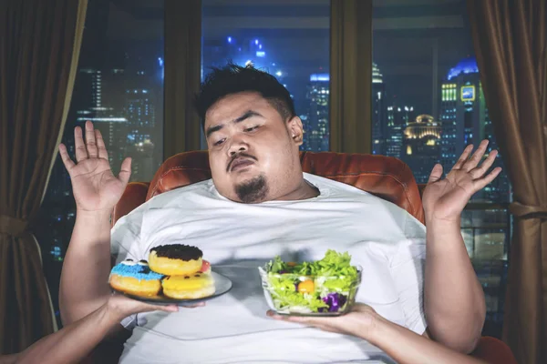 Homem gordo escolhendo alimentos com expressão confusa — Fotografia de Stock