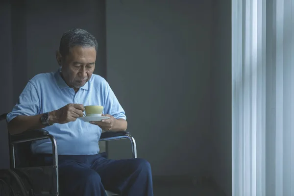 Viejo sosteniendo una taza de té en la silla de ruedas — Foto de Stock