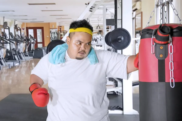 Homem com excesso de peso atinge um saco de boxe no centro de fitness — Fotografia de Stock