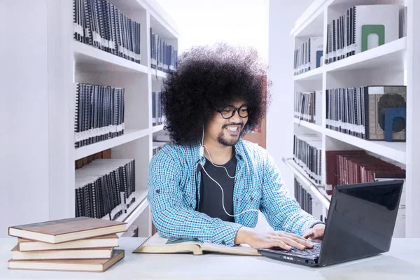 Studente crespo con laptop e auricolare in biblioteca — Foto Stock