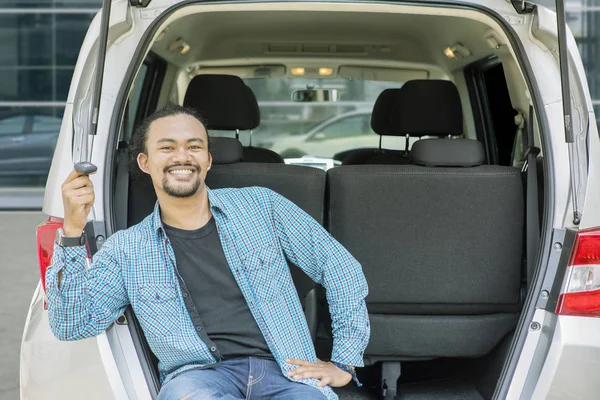 Lycklig ung man innehar en bil nyckel i bilen trunk — Stockfoto