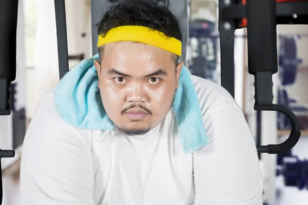 Hombre gordo enojado se sienta en la máquina de ejercicios — Foto de Stock