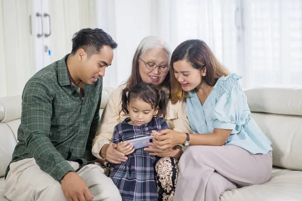 Girl uses phone with parents and grandmother — Stock Photo, Image