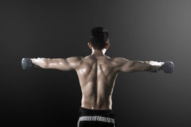 Gömleksiz genç adamın arka görünümü halter leri kaldırıyor