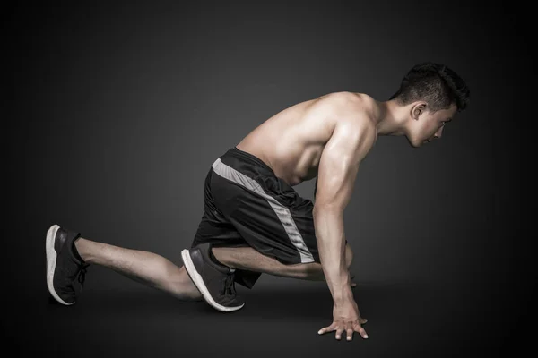 Muscular young man kneeling in the dark room — Stock Photo, Image