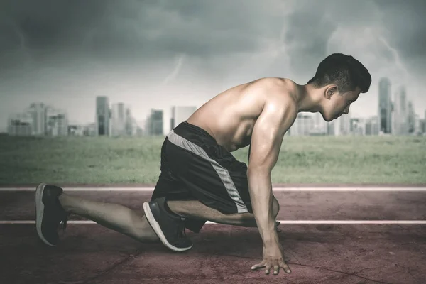 Musculoso joven arrodillado en la pista — Foto de Stock