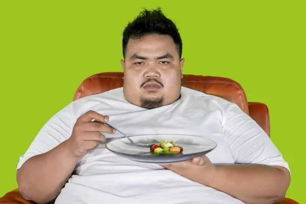 Elhízott ember úgy néz ki, boldogtalan enni saláta stúdióba — Stock Fotó
