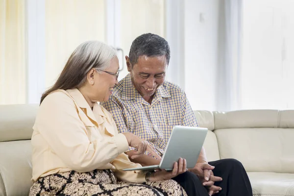 Старшая пара выглядит счастливой с ноутбуком дома — стоковое фото