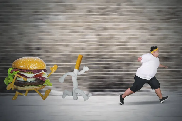 Młody tłuszcz człowiek biegnie od papierosów i Burger — Zdjęcie stockowe