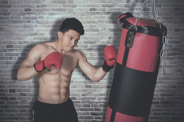 Shirtless young man hits on a boxing bag — Stock Photo, Image