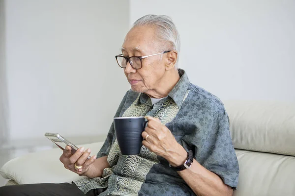 Старший наслаждается отдыхом за чаем и телефоном — стоковое фото