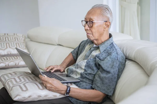 Пожилой человек, использующий ноутбук дома — стоковое фото