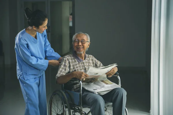 Happy old man sits on a wheelchair with his nurse