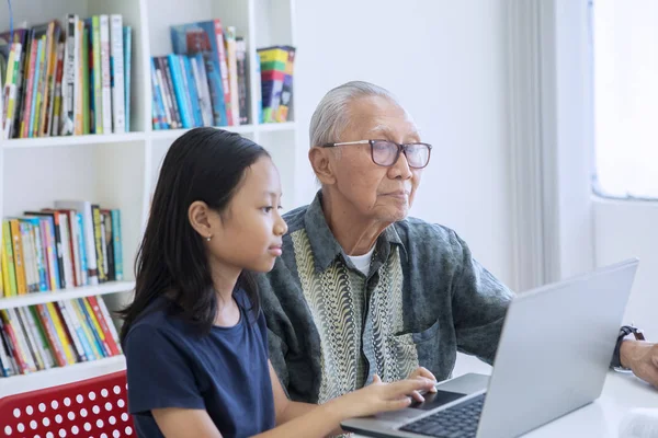 Маленька дівчинка використовує ноутбук зі своїм дідом — стокове фото