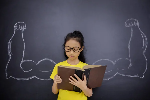 Nerdy schoolgirl shows her biceps in classroom — Stock Photo, Image