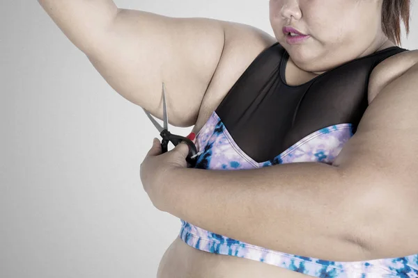 Obese woman cuts her fat upper arm on studio — Stock Photo, Image