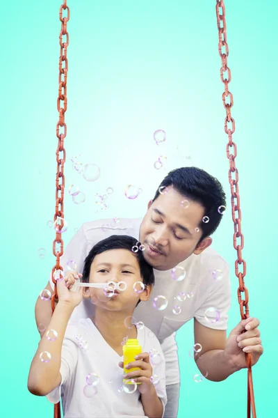 Jovem sopra bolhas de sabão com seu filho — Fotografia de Stock
