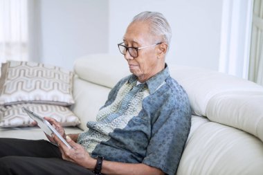 Evde dijital tablet kullanan yaşlı adam