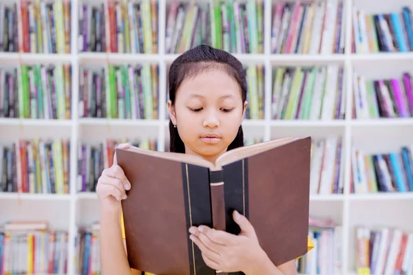 Chytrá školka četla knihu v knihovně. — Stock fotografie