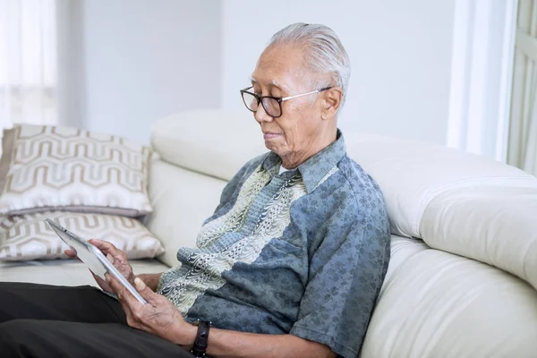 Пожилой человек, использующий цифровой планшет дома — стоковое фото