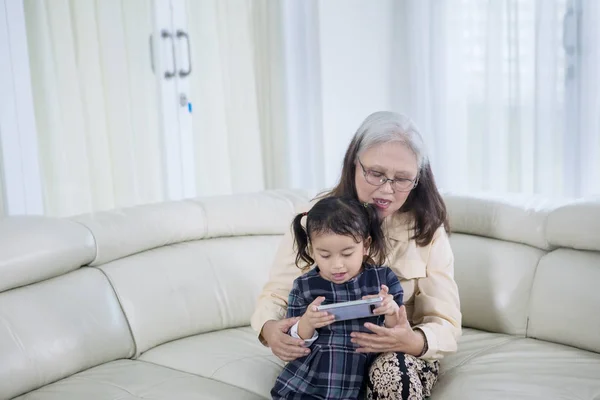 Oudere vrouw met behulp van een telefoon met haar kleinkind — Stockfoto