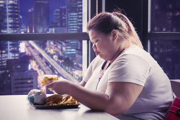 Mujer con sobrepeso come comida chatarra en la cafetería por la noche — Foto de Stock