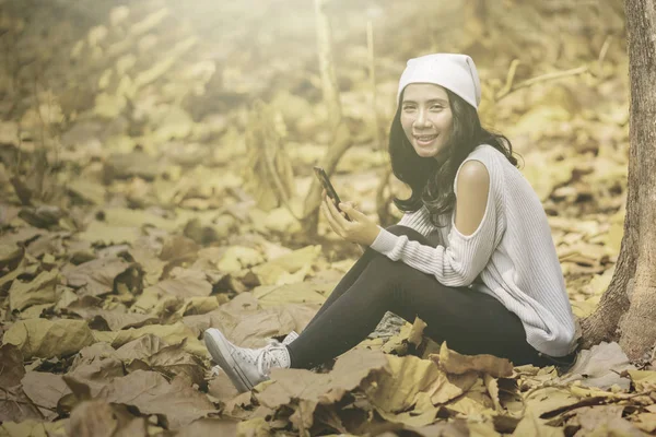 Kadın cep telefonu ile sonbahar parkta oturur — Stok fotoğraf