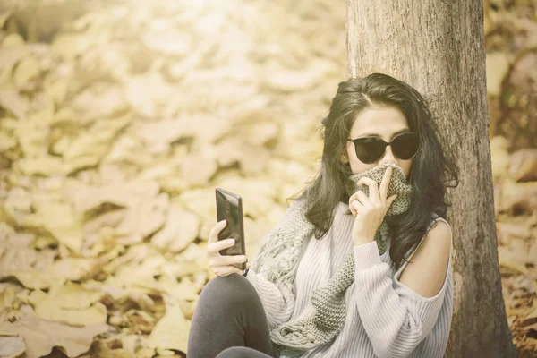 Жінка сидить в осінньому парку з мобільним телефоном — стокове фото