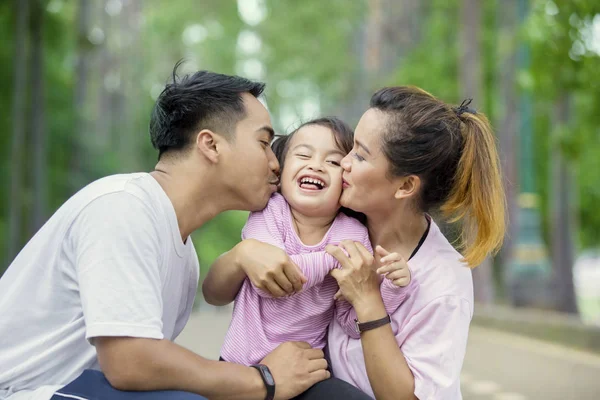 Padres jóvenes besando a su hija en el parque —  Fotos de Stock