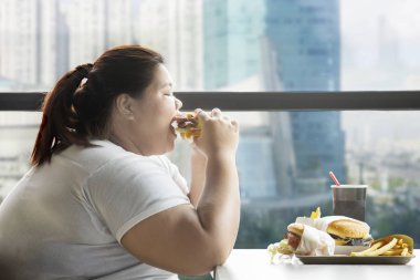 Açgözlü şişman kadın restoranda bir burger yemek