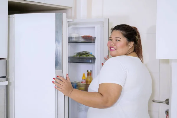 Товста жінка спіймана червоною рукою перевіряє холодильник — стокове фото
