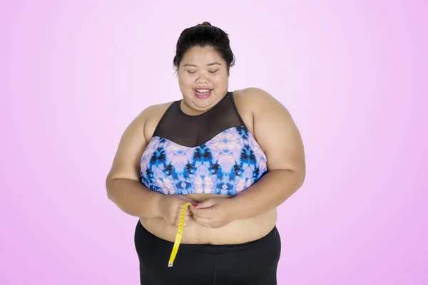 Happy fat woman measuring her waistline on studio — Stock Photo, Image