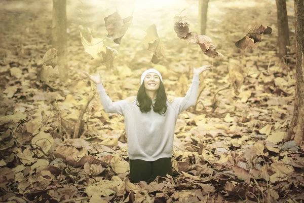Χαρούμενη γυναίκα που πετάει αποξηραμένα φθινοπωρινά φύλλα στο πάρκο — Φωτογραφία Αρχείου
