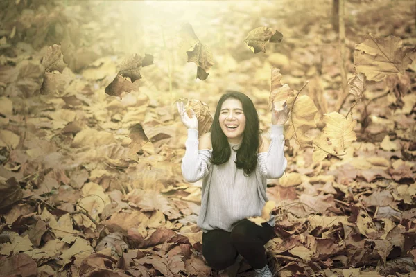 Mujer alegre lanzando hojas secas de otoño al parque — Foto de Stock