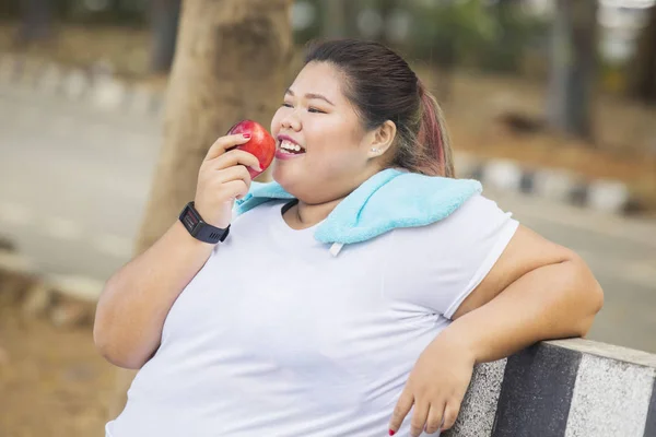 Übergewichtige Frau isst nach Sport im Park Apfel — Stockfoto