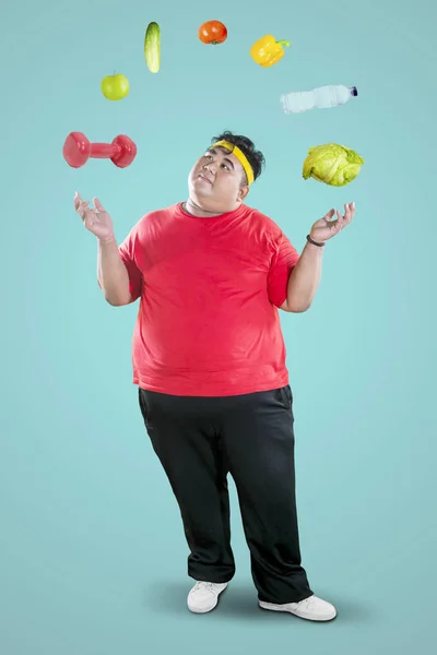 Overweight man juggling dumbbell and foodstuff — Stock Photo, Image