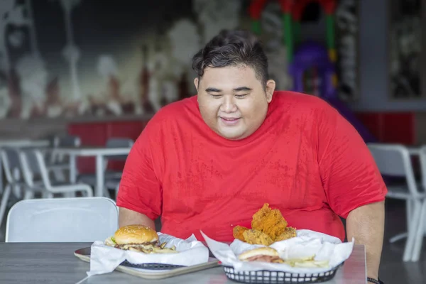 Hombre con sobrepeso mirando comida chatarra en la mesa — Foto de Stock