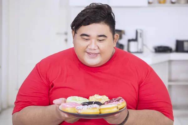 Hombre con sobrepeso se ve feliz de comer rosquillas sabrosas — Foto de Stock