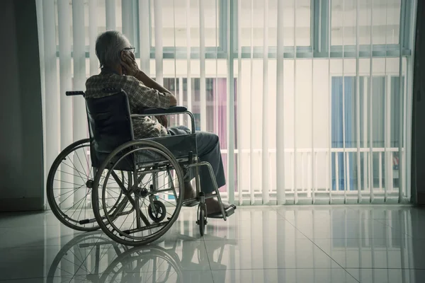 Homme âgé regardant par la fenêtre dans un fauteuil roulant — Photo