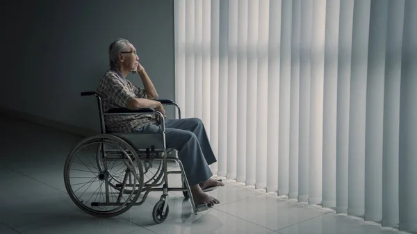 Hombre mayor se sienta en la silla de ruedas cerca de la ventana — Foto de Stock