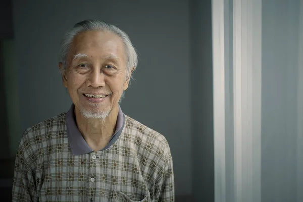 Smiling elderly man standing near the window — Stock Photo, Image