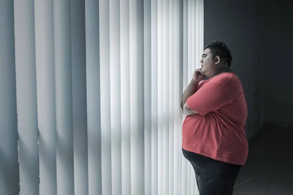 Jovem gordo a pensar em algo perto da janela — Fotografia de Stock