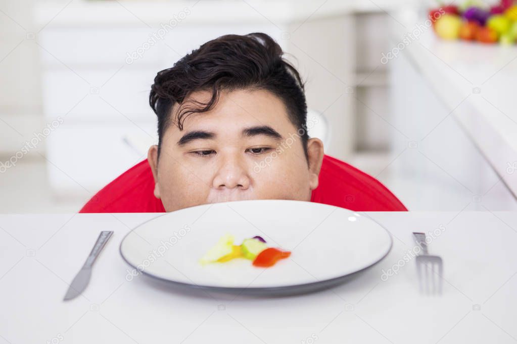 Young fat man peeking out salad of the table