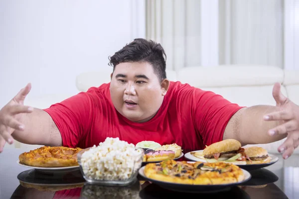 Genç obez adam yiyecek çok yemek için cazip görünüyor — Stok fotoğraf