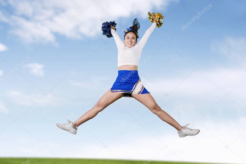Beautiful cheerleader girl doing splits in meadow